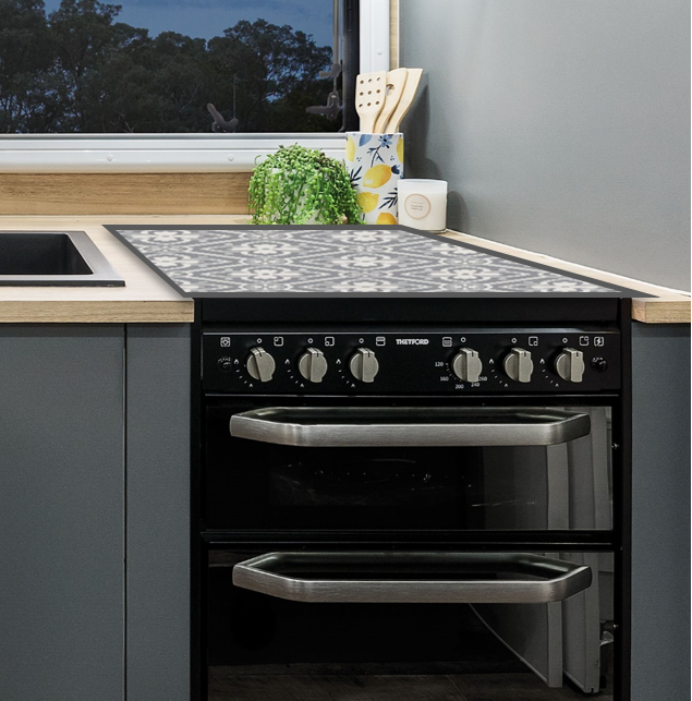 A vinyl cooker cover placed on a cooktop within a caravan kitchen setting, predominantly grey in color.